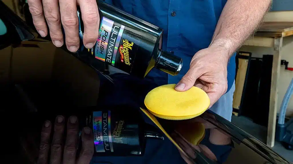 A person applying Meguiar's Ultimate Best Polish on a yellow sponge