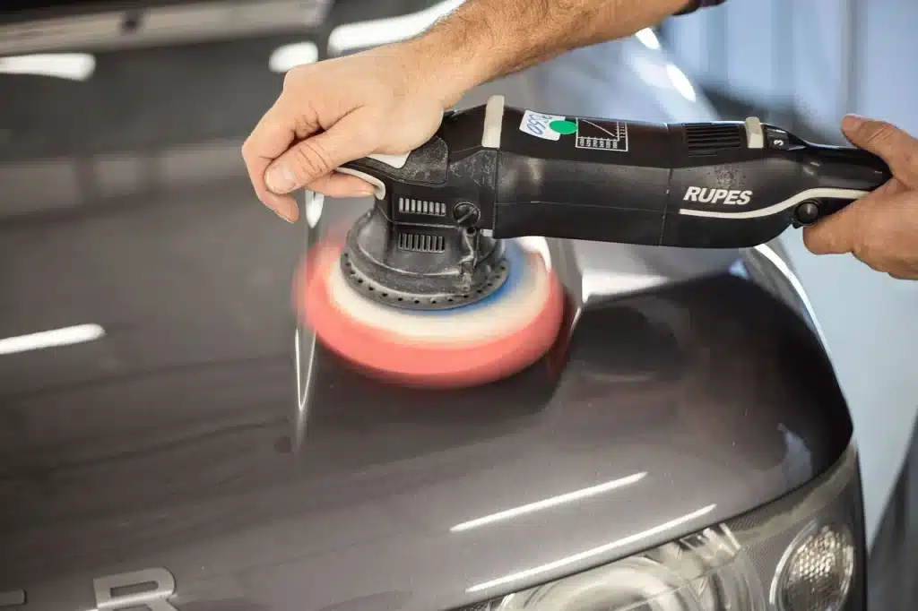 A person applying car polish on a car with a polishing machine