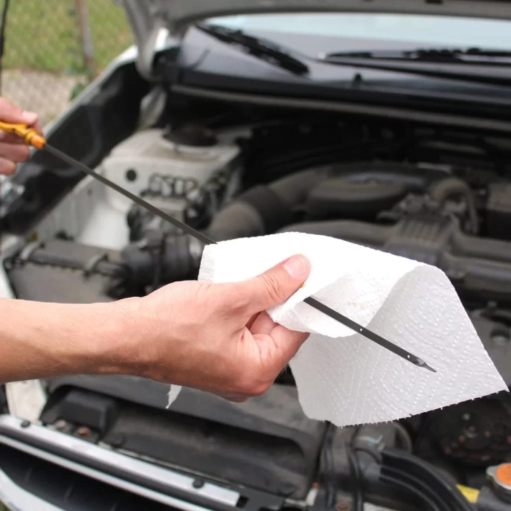 A person checking oil in a car with a stick by a tissue paper