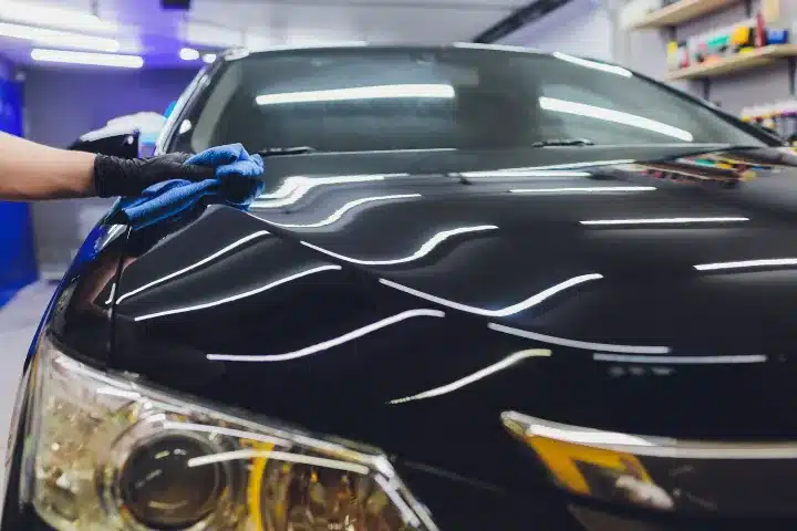 A person cleaning a shiny polished black car