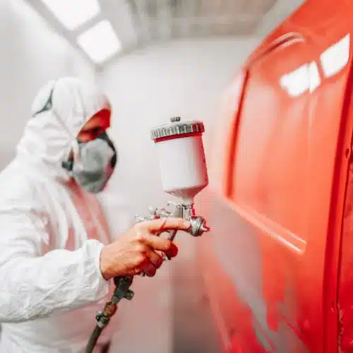 A person spray painting an orange car