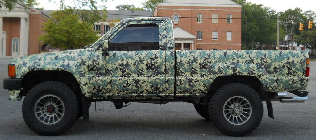 A side view of a car truck outside a house with a digital camouflage car wrap
