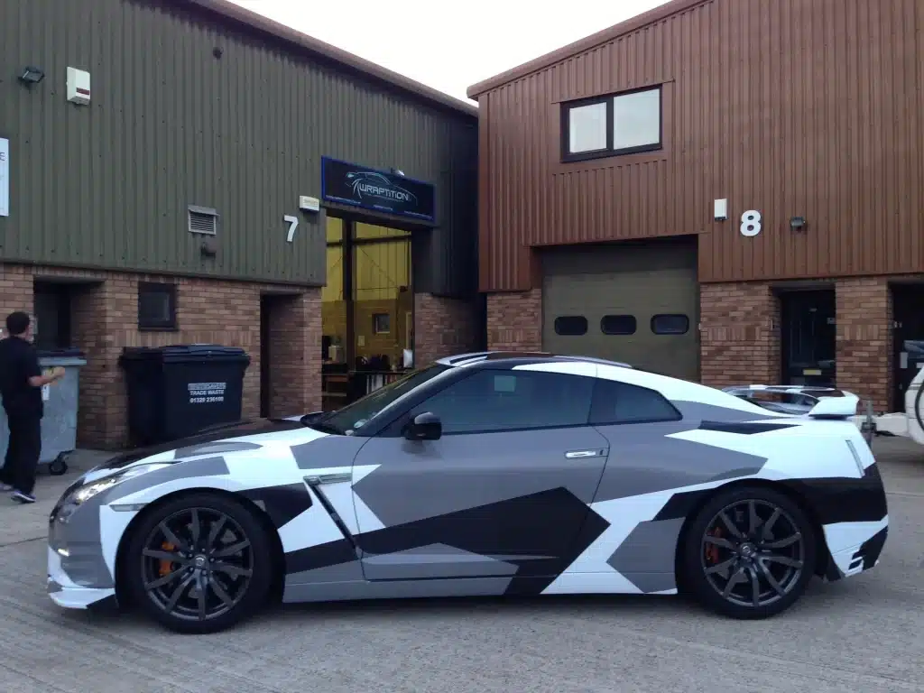 A side view of a car with black grey and white abstract car wrap art outside a garage