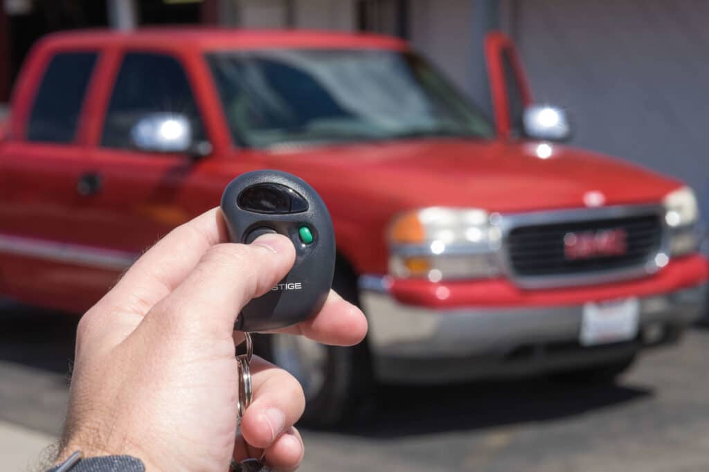 A view of a person holding a car key for alarm beeping with a blurred red car in view