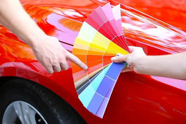 Two hands holding a color chart to match color over a red car
