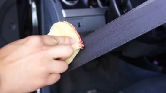 A person cleaning the car seatblet with a cloth