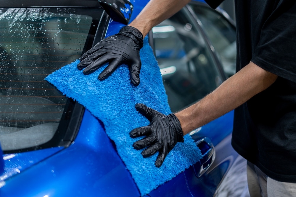 A view of a person drying a blue car with a towel