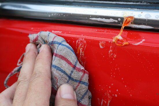A view of a person removing sticky sap off a red car with a cloth