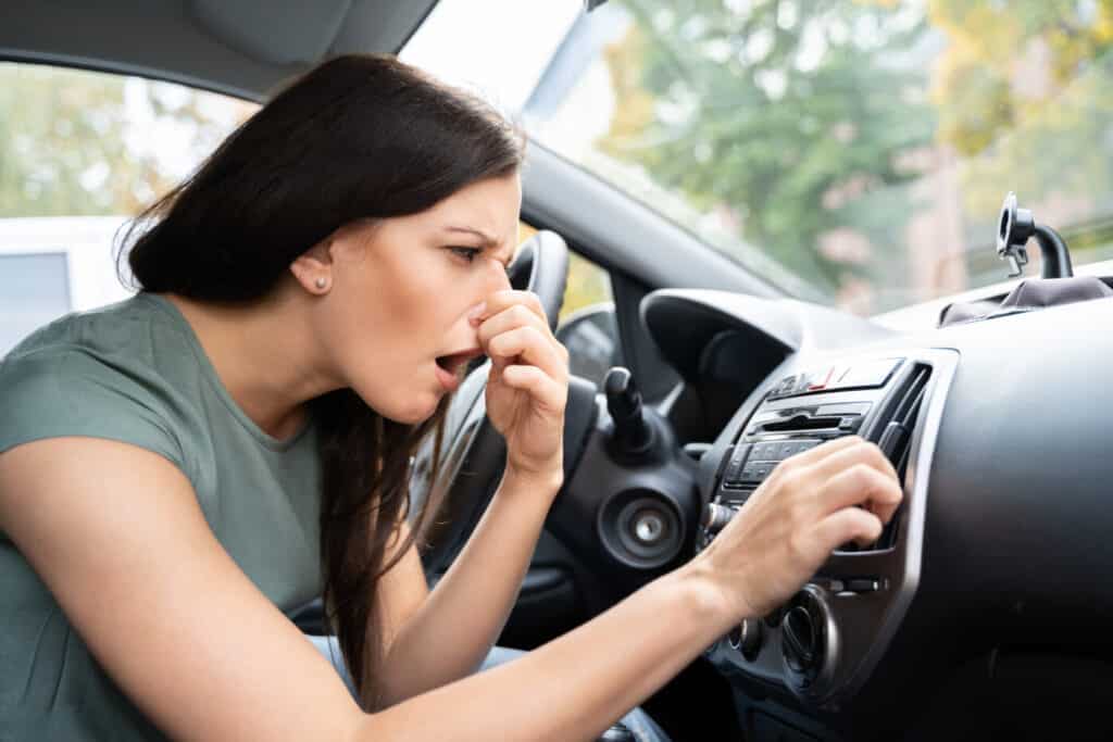 A woman holding her nose due to bad smoke odor inside a car