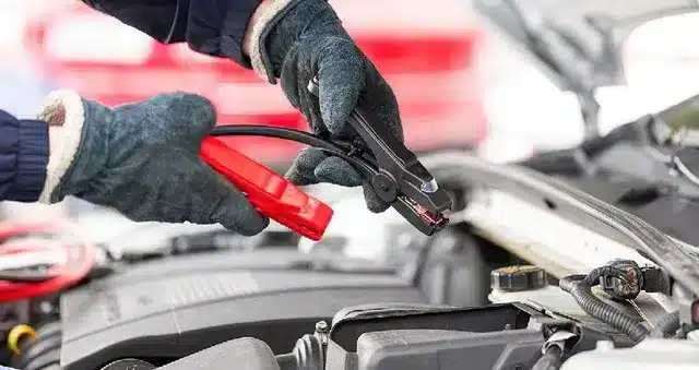 a man wearing gloves and hilding jumper cables in his hand to jumpstart a car