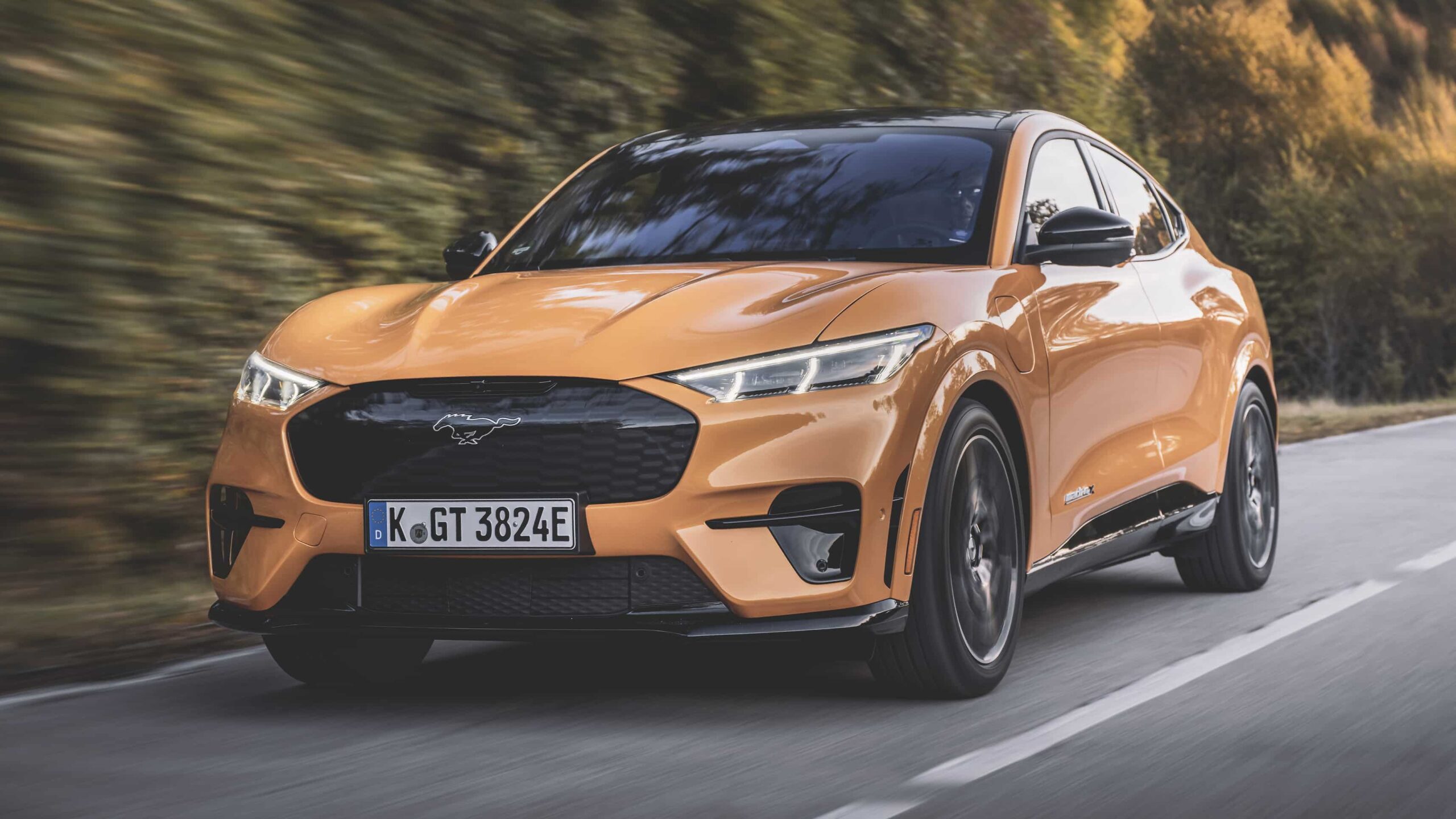 A front view of an orange ford mustang mach e speeding on road