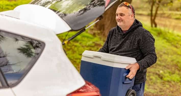 A view of a man holding a cooler to keep it inside thge car back