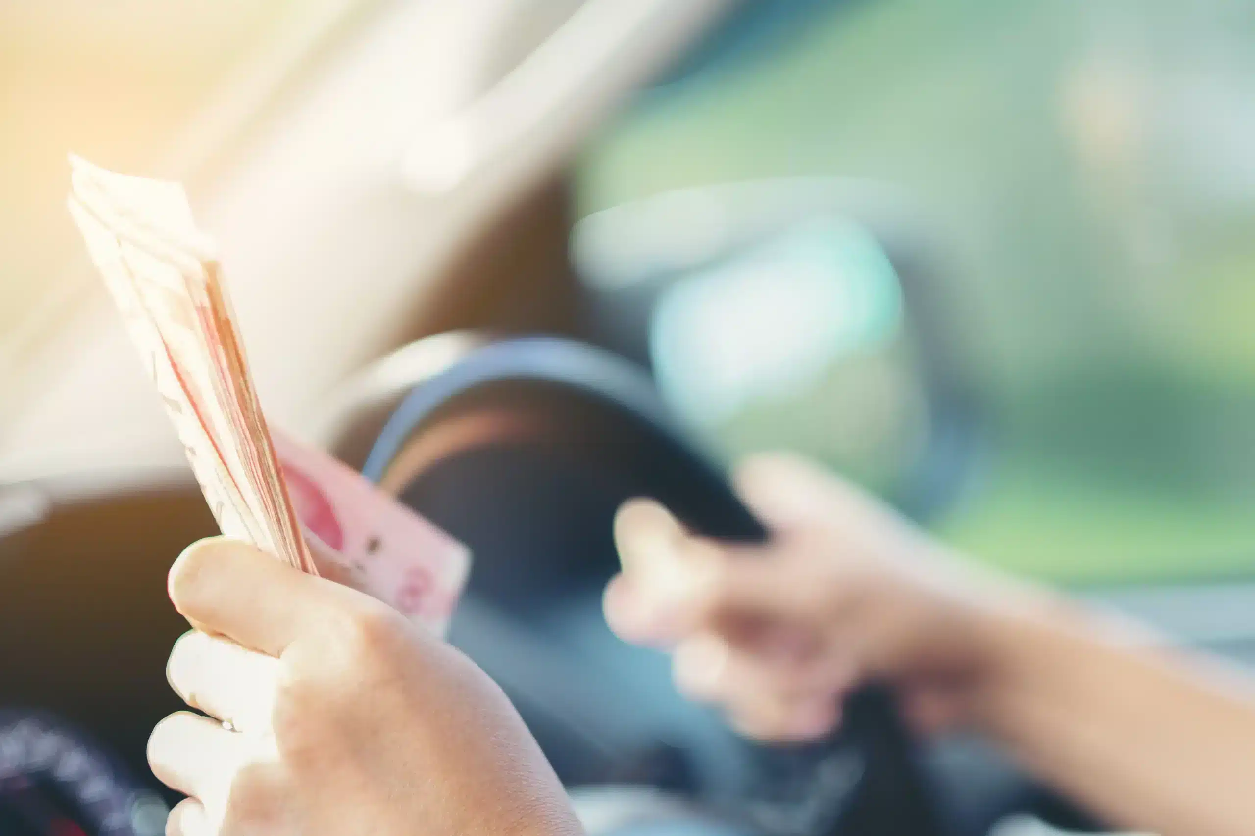 A view of a person driving a car and holding money in one hand