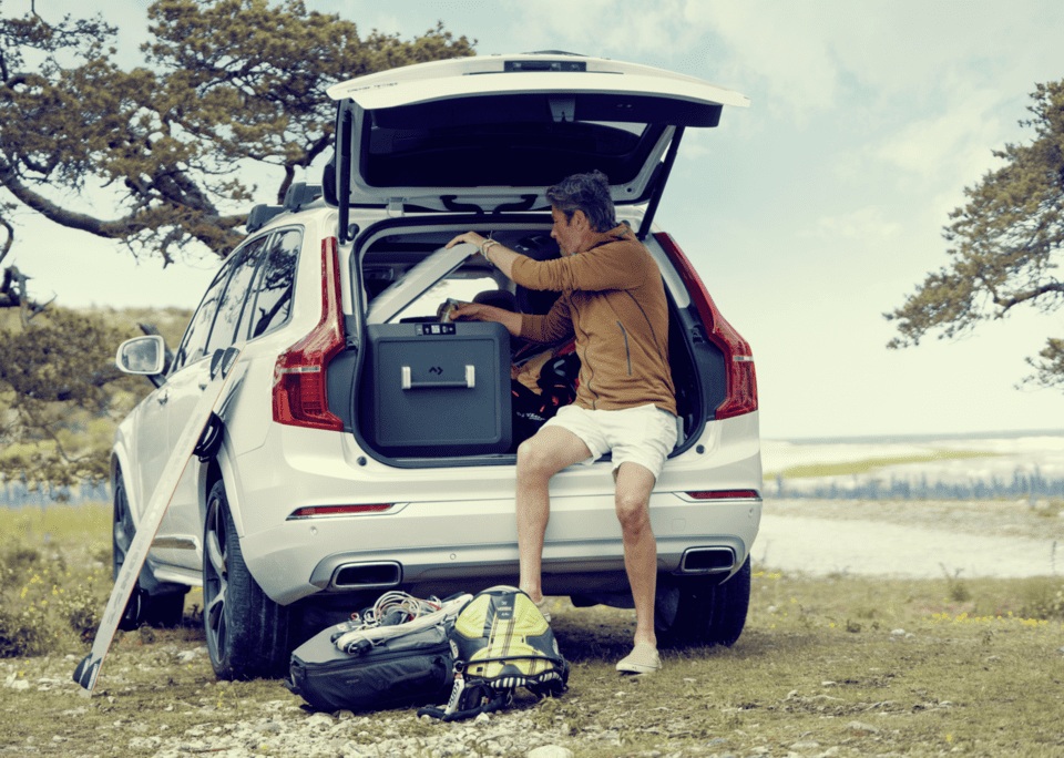 A view of a man holding a cooler to keep it inside thge car back