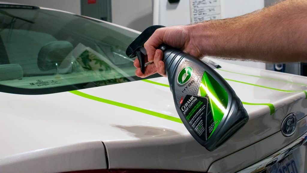 A view of a person spraying ceramic coating over a white car