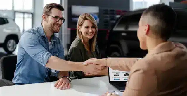 A view of two guys shaking hands closing a car lien deal with a girl sititng behind