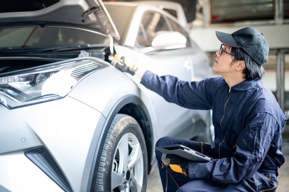 A side view of a mechanic inspecting a silver car