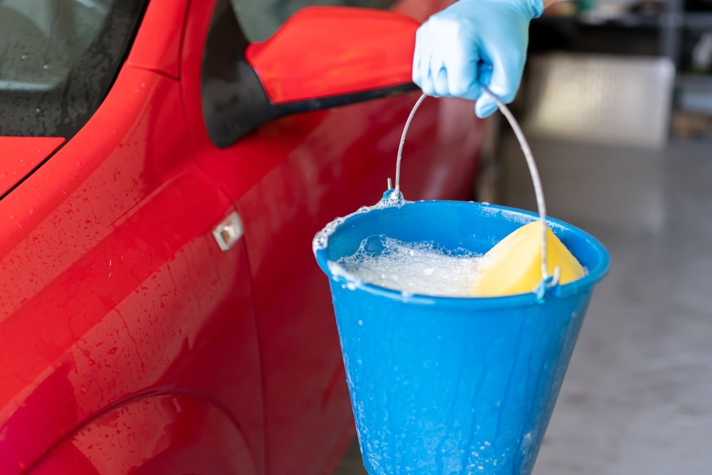 A view of a perosn holding a bucket of car wash soap