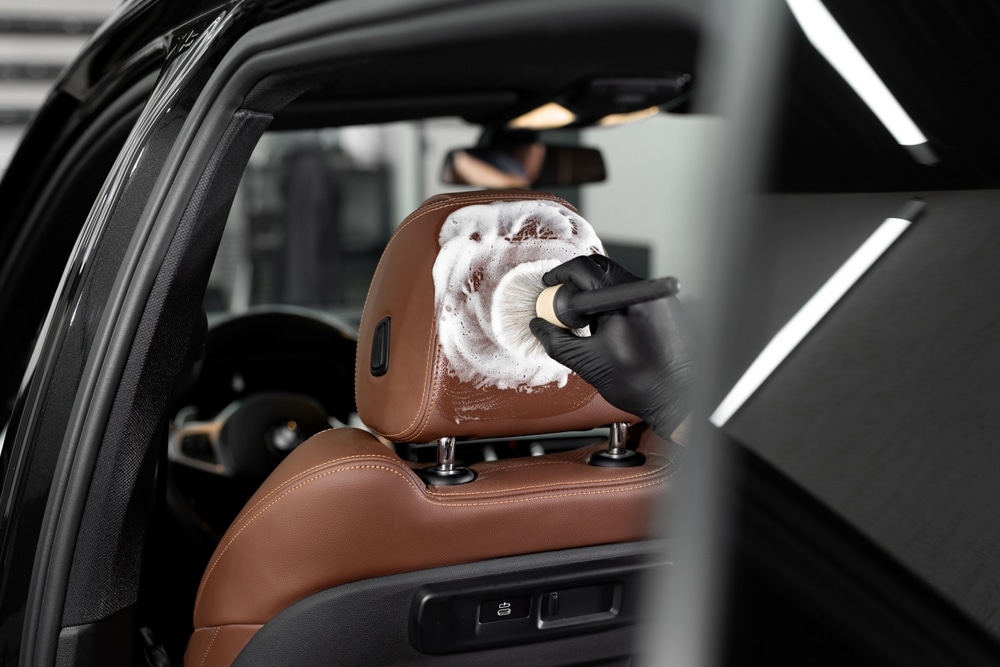 A view of a person cleaning the back of a car seat with a soap and brush