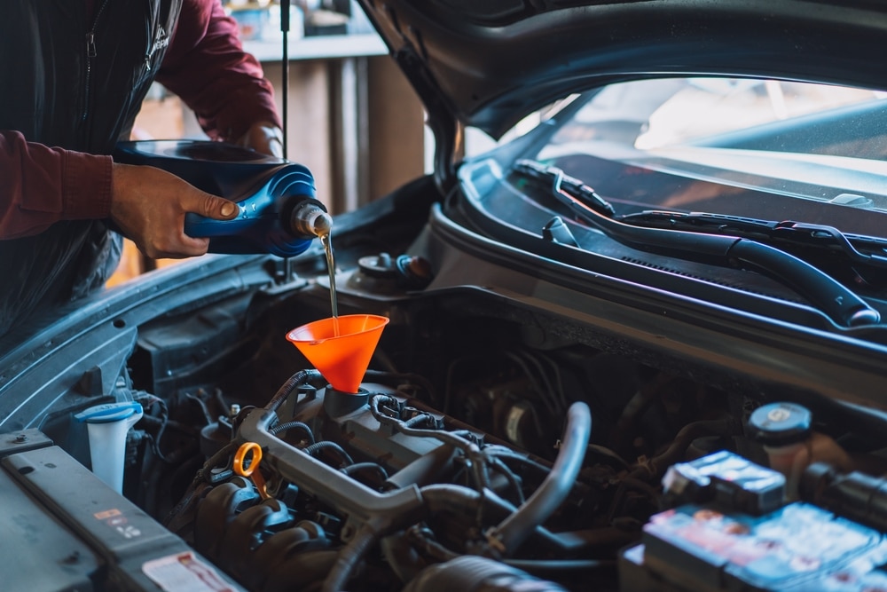 A view of a person adding to a car engine with a funnel