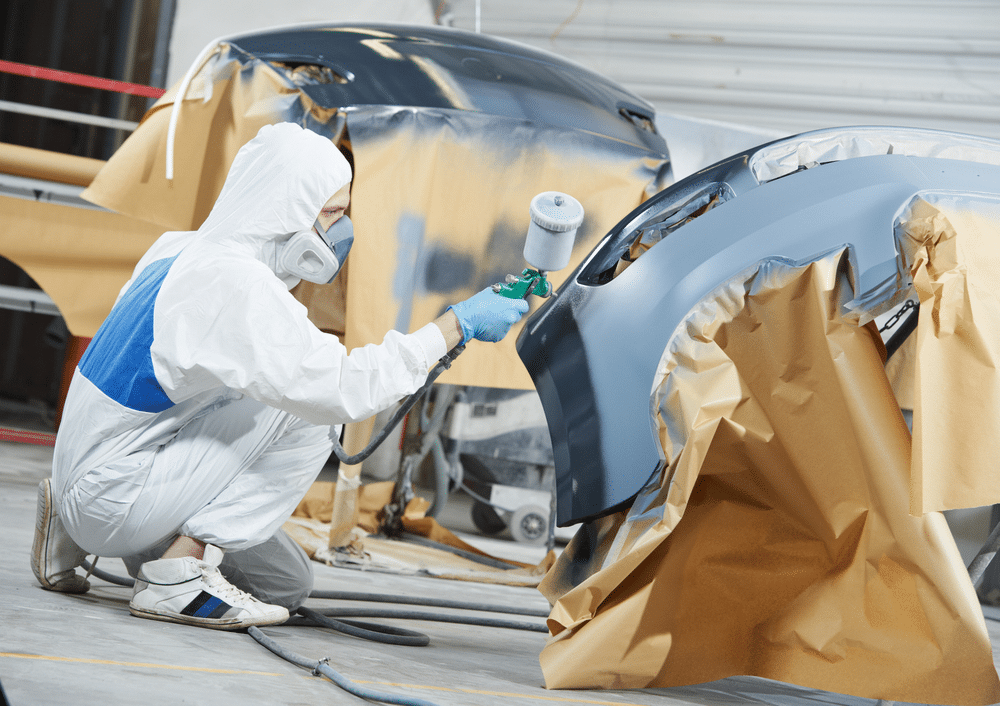 A view of an auto mechanic spraying a car bumper